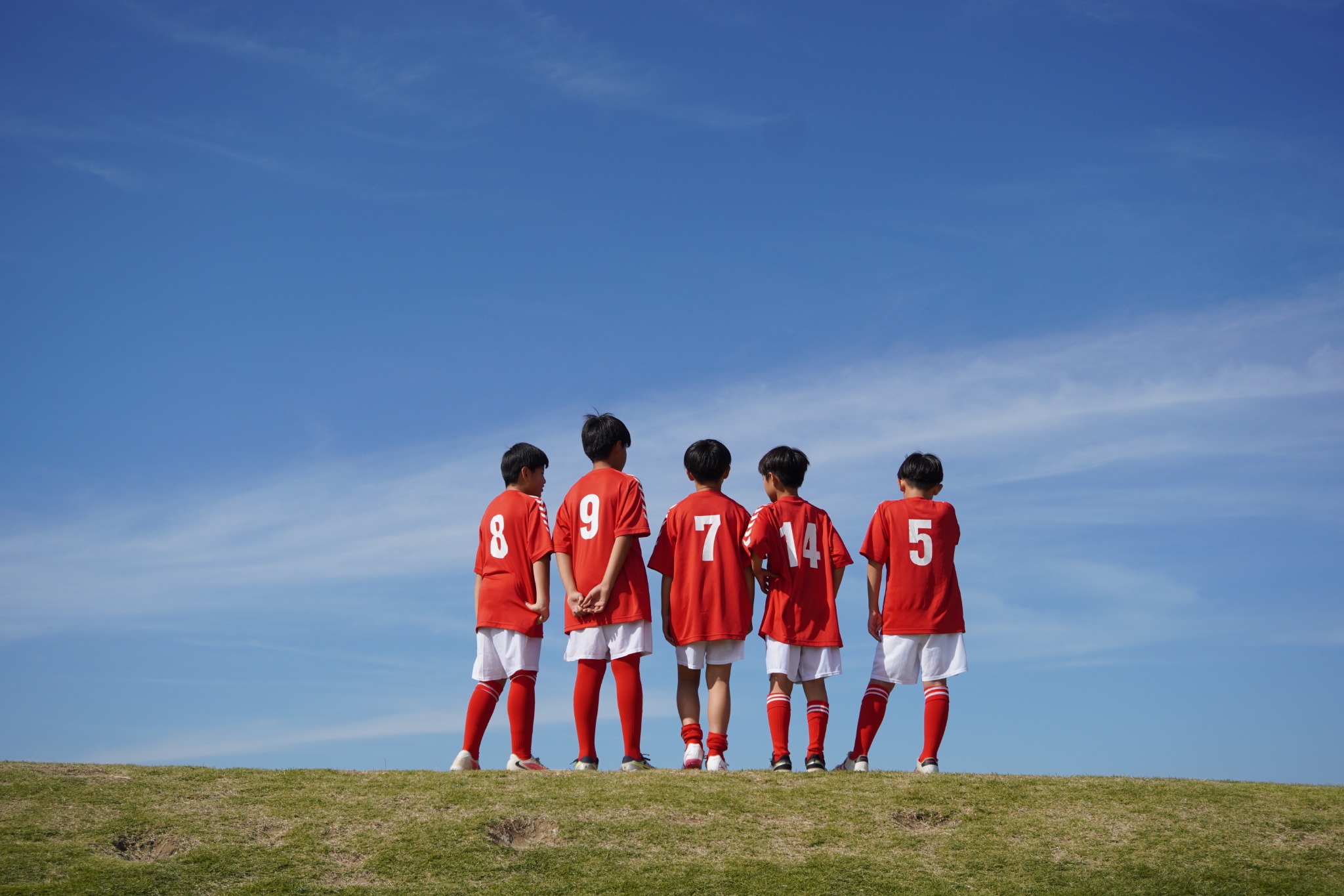 青空の下、赤いユニフォームを着て並ぶ谷田部FCの仲間たち